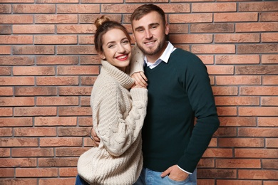 Photo of Young couple in warm sweaters near brick wall