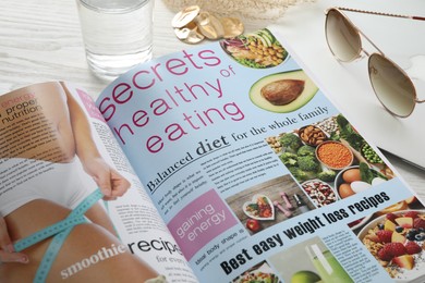 Photo of Open healthy food magazine, laptop and accessories on table, closeup