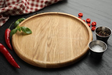 Photo of Cutting board, salt, spices, basil and chili peppers on black textured table. Space for text