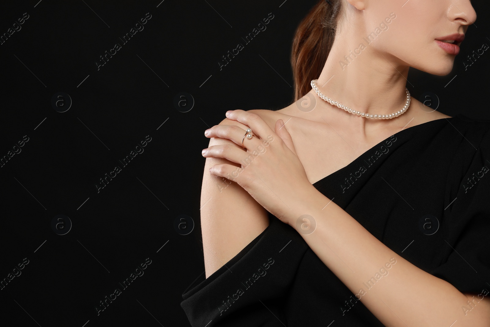 Photo of Young woman wearing elegant pearl jewelry on black background, closeup. Space for text