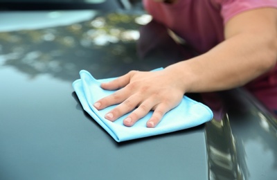 Photo of Young man washing car hood with rag outdoors, closeup