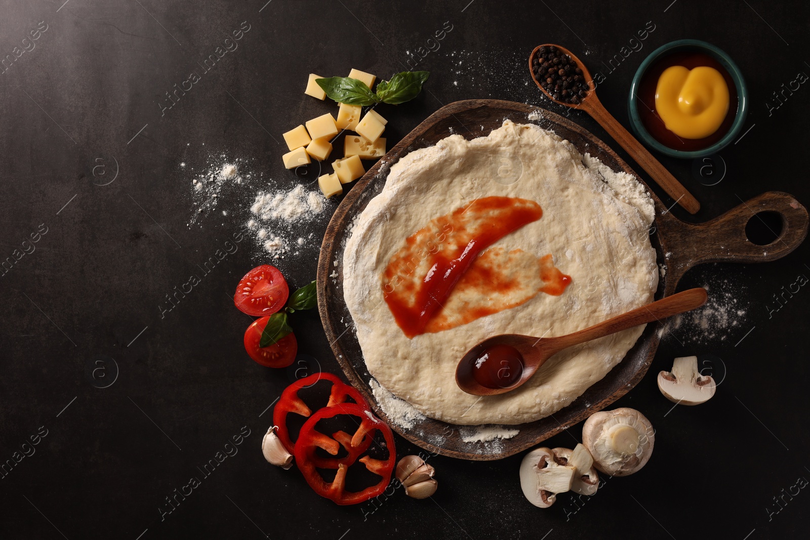 Photo of Pizza dough with tomato sauce and products on dark table, flat lay. Space for text