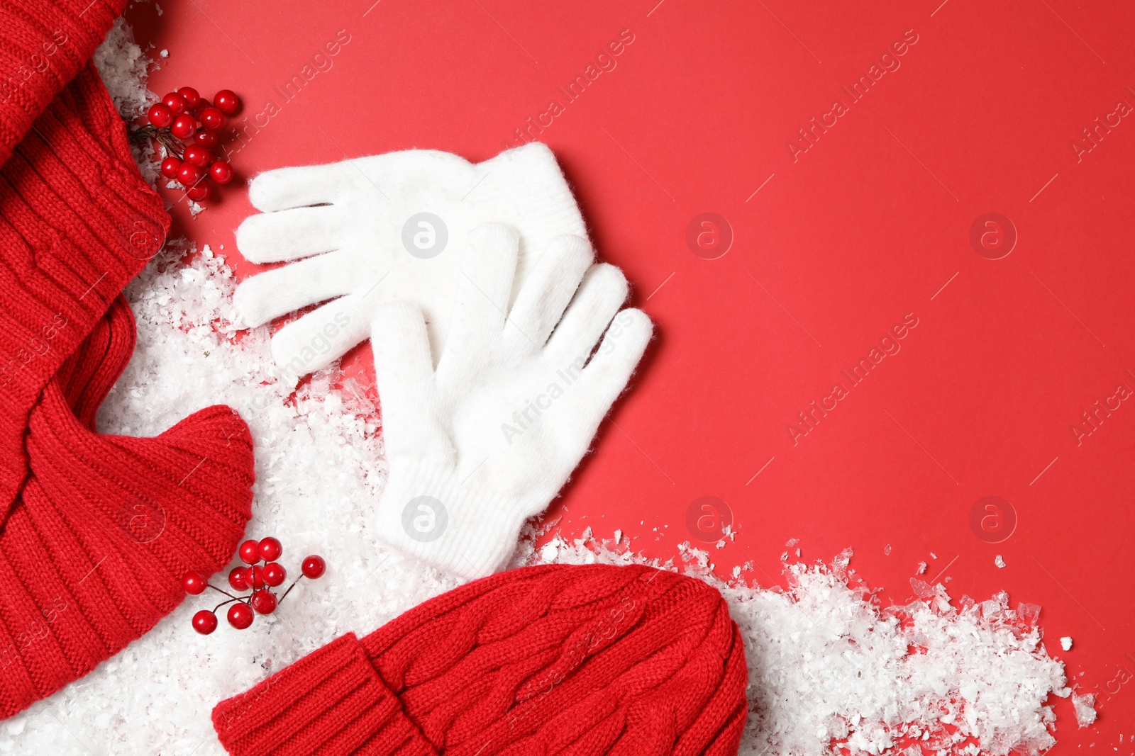 Photo of Stylish white woolen gloves, hat, scarf and winter decor on red background, flat lay. Space for text