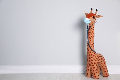 Toy giraffe with face mask and stethoscope near white wall, space for text. Pediatrician practice