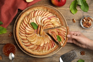 Photo of Woman taking slice of apple pie at wooden table, top view