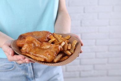 Photo of Woman holding fish and chips in paper plate on near white brick wall, closeup. Space for text