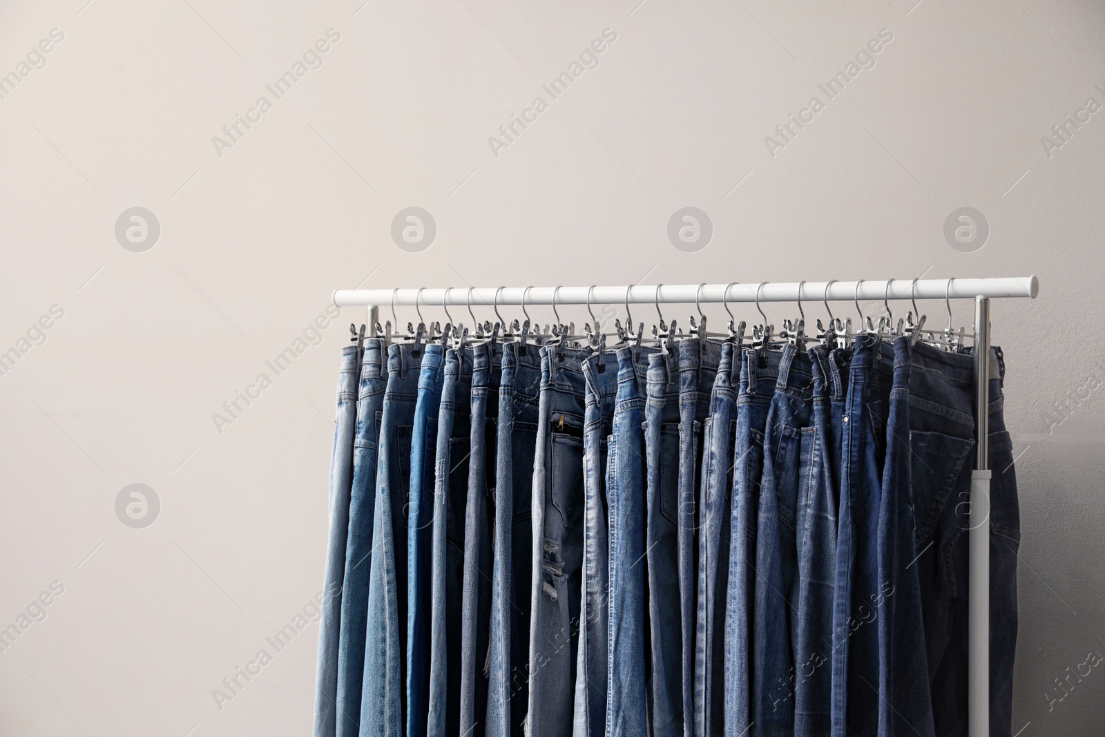 Photo of Rack with stylish jeans on beige background