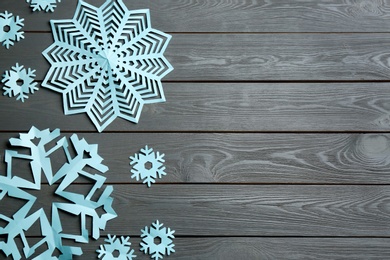 Many paper snowflakes on grey wooden background, flat lay. Space for text