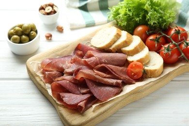 Photo of Board with delicious bresaola served with bread and tomato on white wooden table