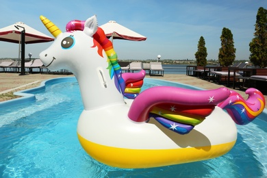 Funny inflatable unicorn ring floating in swimming pool on sunny day, outdoors