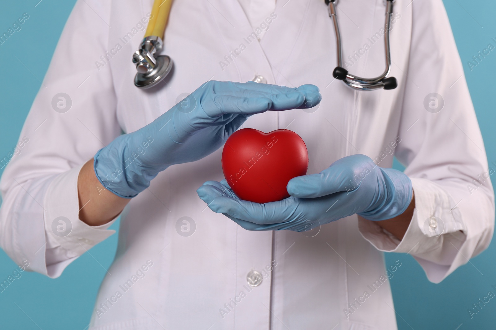 Photo of Doctor with stethoscope and red heart on light blue background, closeup. Cardiology concept