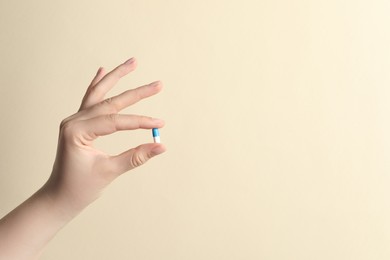 Photo of Woman holding pill on beige background, closeup. Space for text