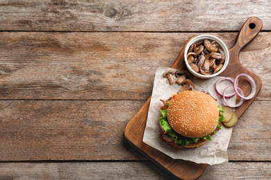 Photo of Tasty burger and mushrooms on wooden background, top view. Space for text
