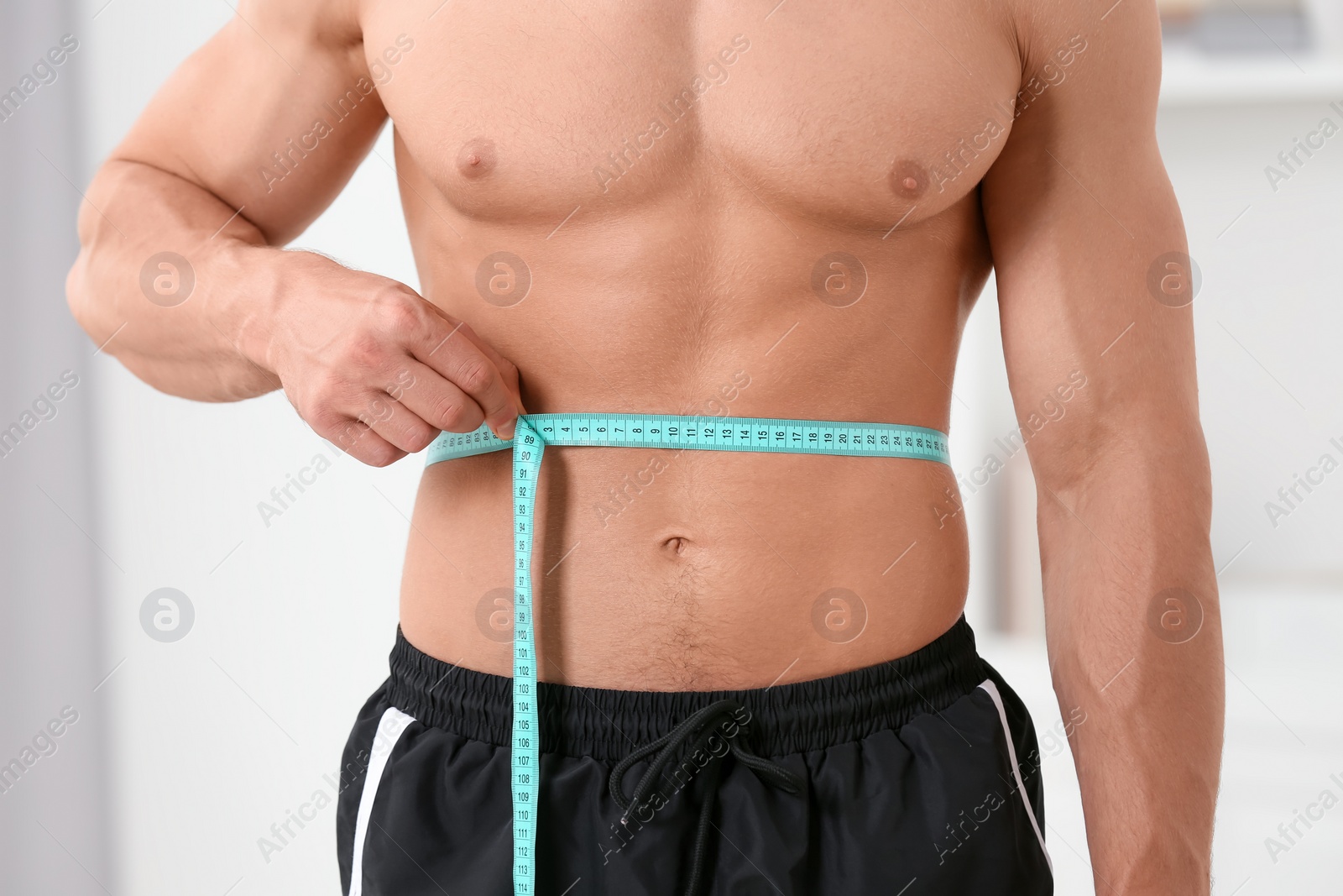 Photo of Athletic man measuring waist with tape at home, closeup. Weight loss concept