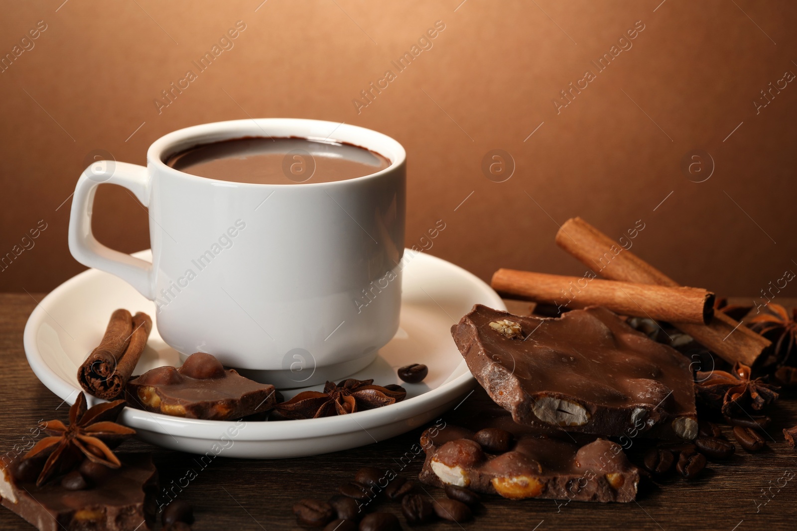 Photo of Cup of delicious hot chocolate, spices and coffee beans on wooden table