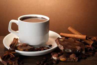 Cup of delicious hot chocolate, spices and coffee beans on wooden table