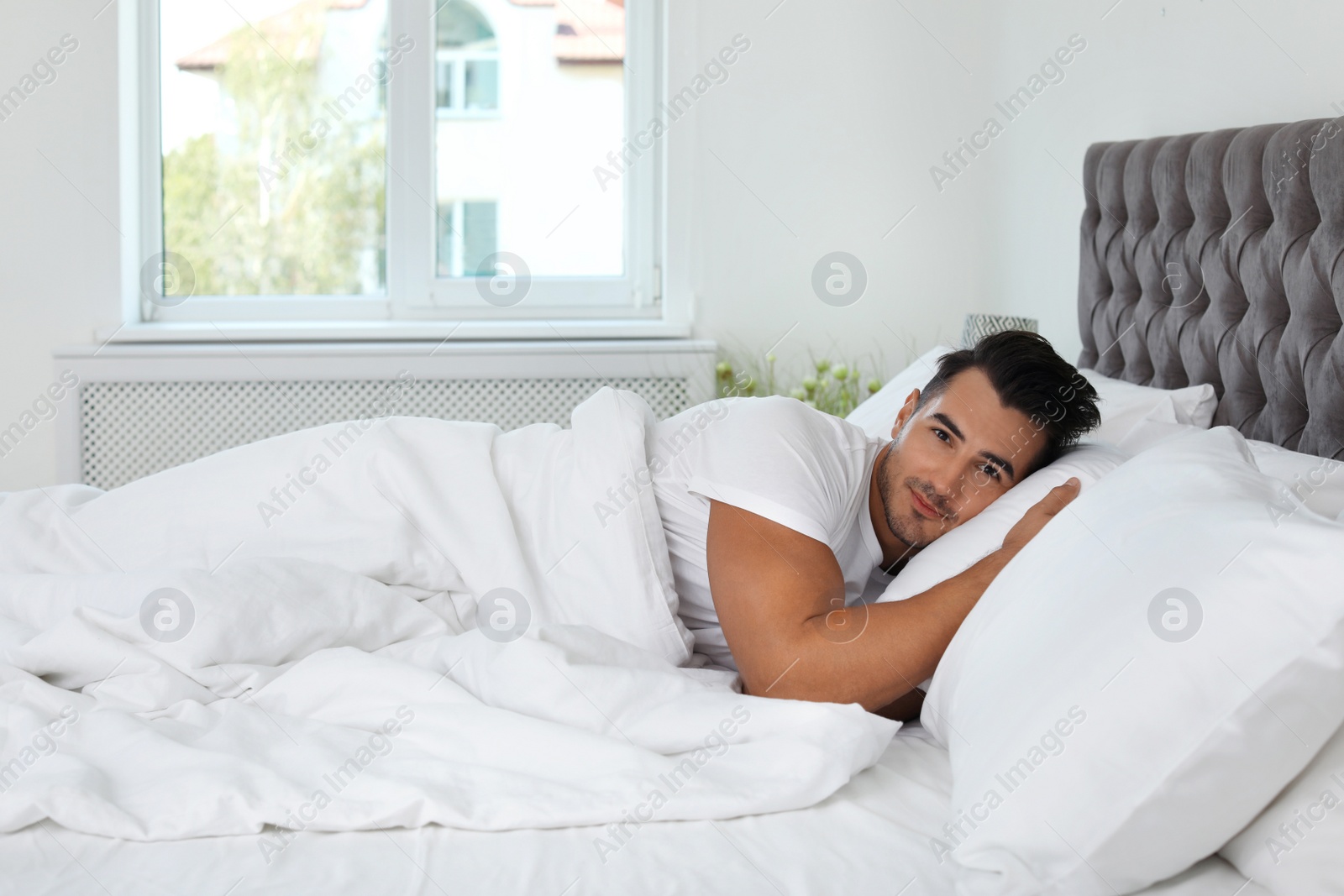 Photo of Young man lying in bed with soft pillows at home