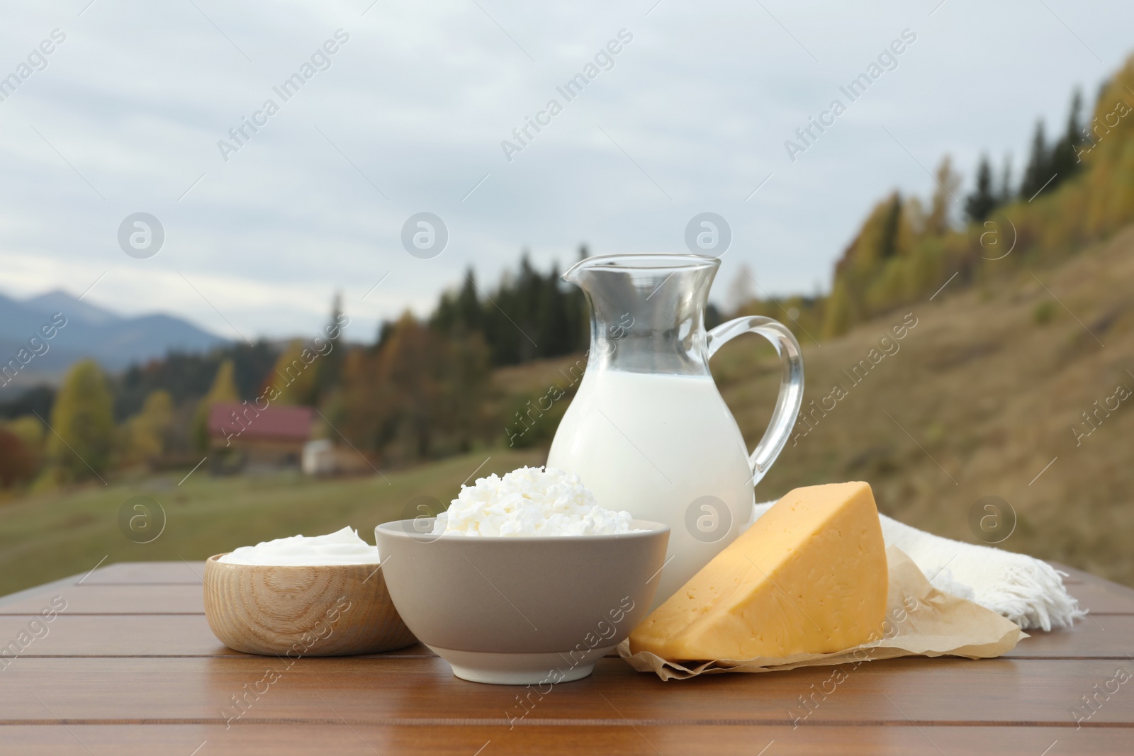 Photo of Tasty cottage cheese and other fresh dairy products on wooden table in mountains