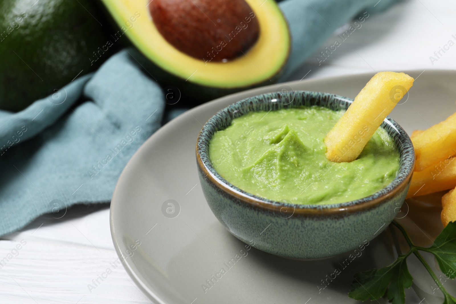 Photo of Plate with french fries, guacamole dip, parsley and avocado served on white wooden table, closeup