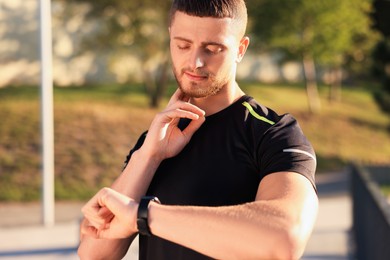 Photo of Attractive serious man checking pulse after training in park