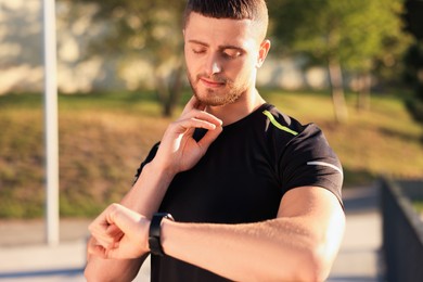 Attractive serious man checking pulse after training in park