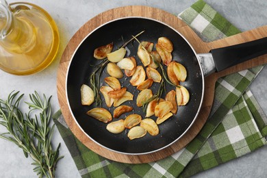 Photo of Frying pan with fried garlic cloves, rosemary and oil on gray table, flat lay