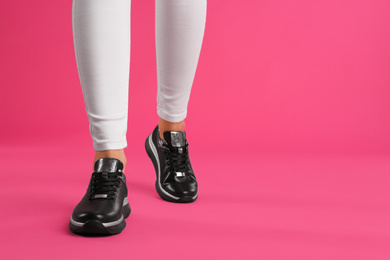 Photo of Woman wearing sneakers on pink background, closeup. Space for text