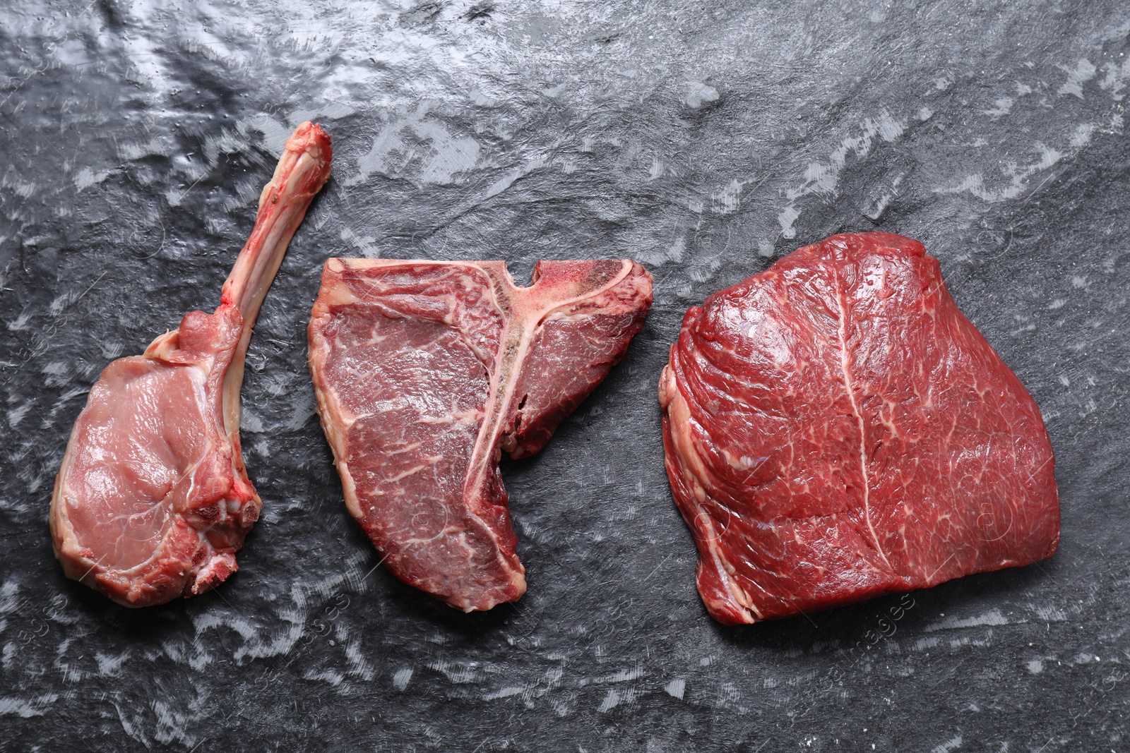 Photo of Fresh raw beef cuts on grey textured table, flat lay