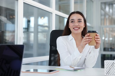 Happy woman with paper cup of coffee at desk in open plan office