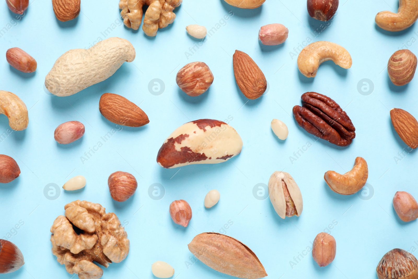 Photo of Different delicious nuts on light blue background, flat lay