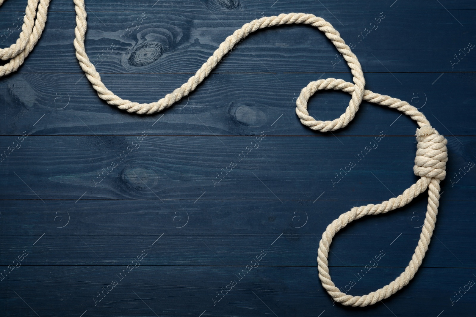 Photo of Rope noose with knot on blue wooden table, top view. Space for text