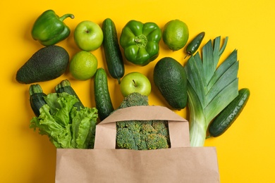 Paper bag with different groceries on yellow background, flat lay