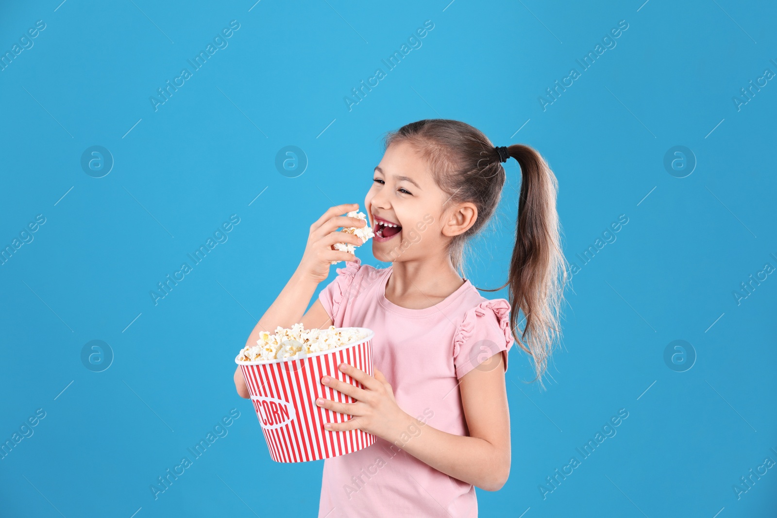 Photo of Cute little girl with popcorn on color background