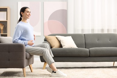 Photo of Happy pregnant woman on armchair at home, space for text