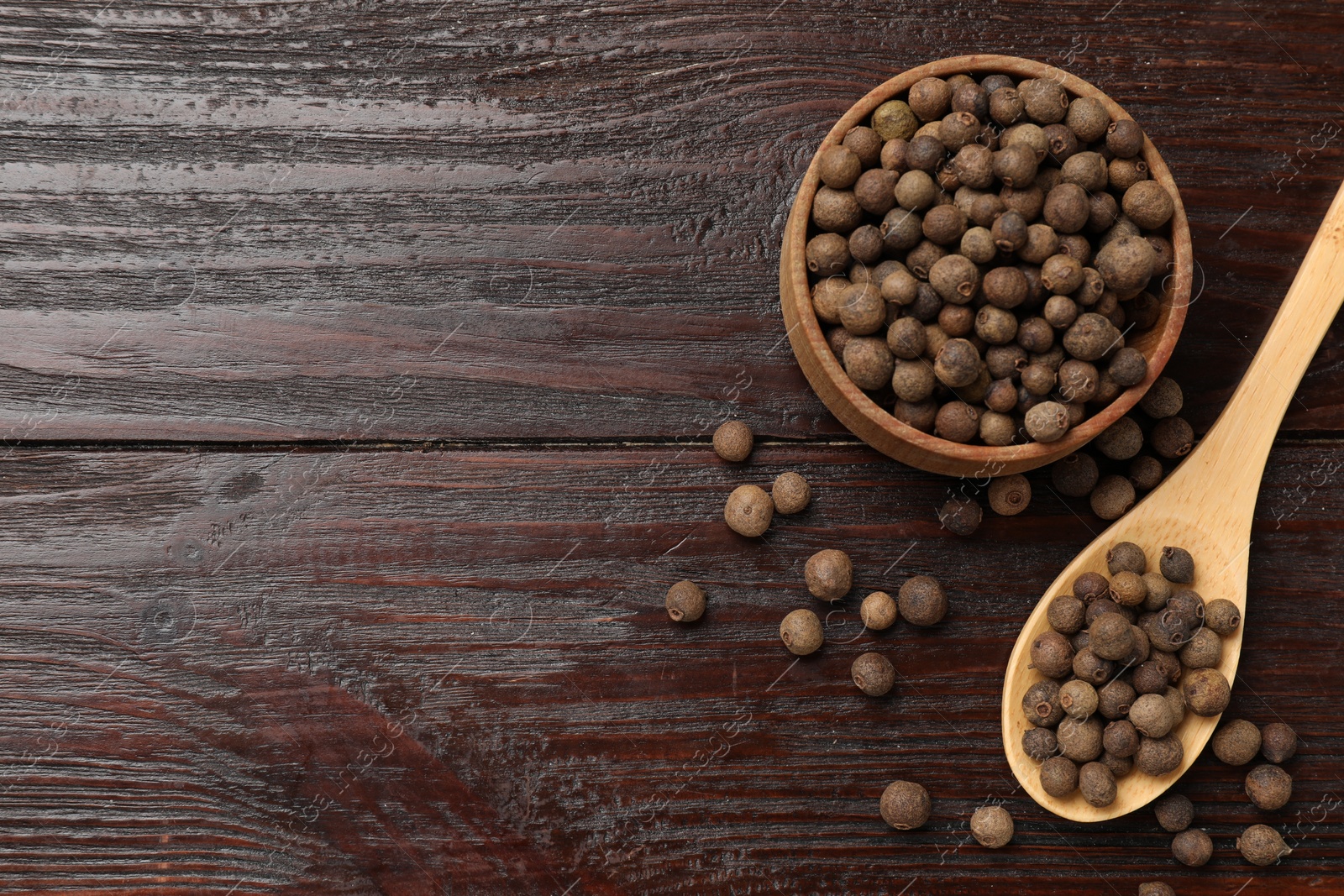 Photo of Dry allspice berries (Jamaica pepper) in bowl and spoon on wooden table, flat lay. Space for text