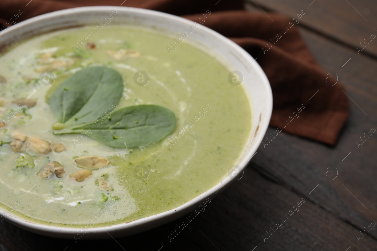 Photo of Delicious broccoli cream soup with basil and pumpkin seeds on wooden table, closeup