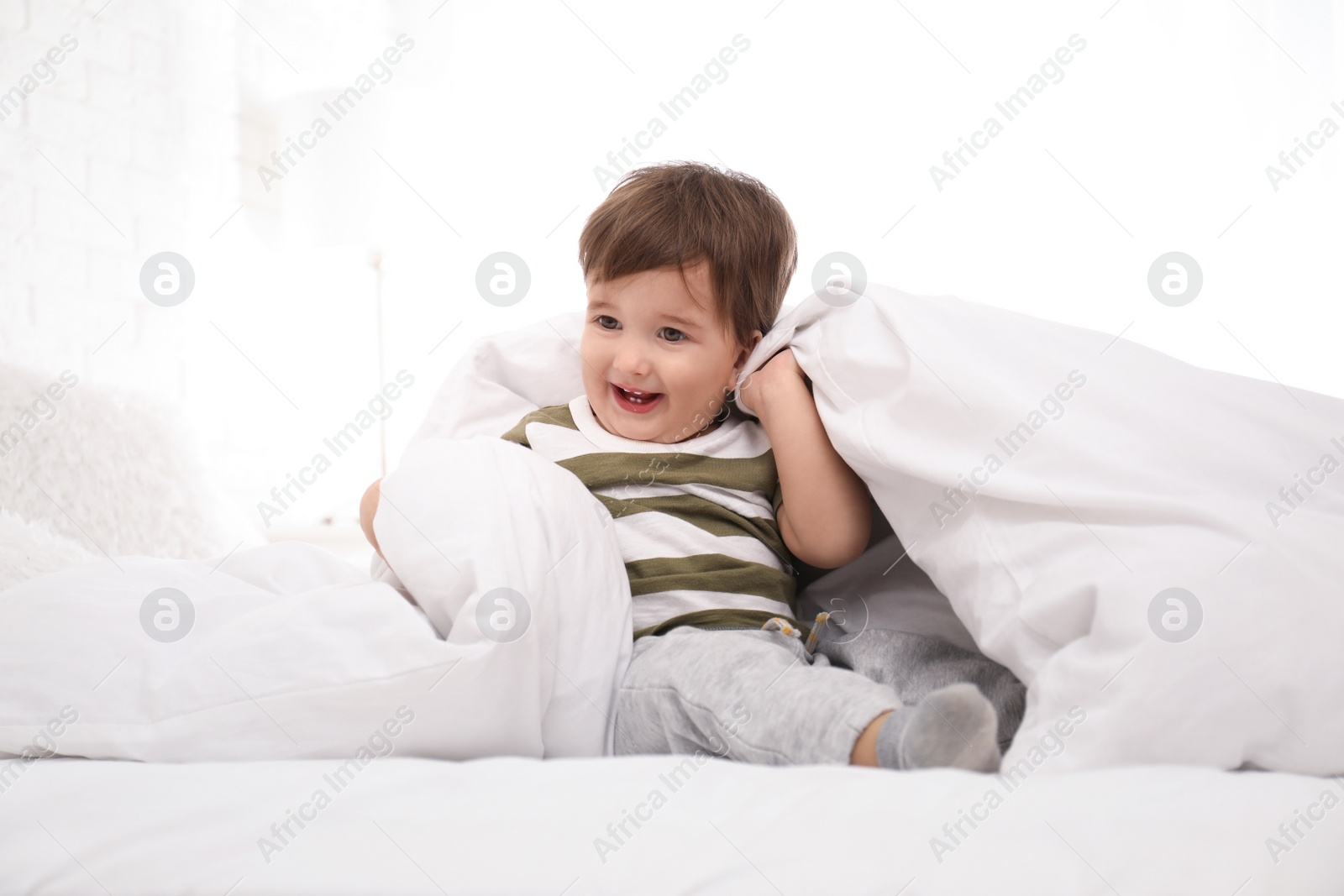 Photo of Cute little child playing under blanket in bed