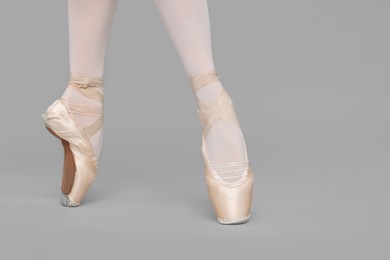 Photo of Young ballerina in pointe shoes practicing dance moves on grey background, closeup
