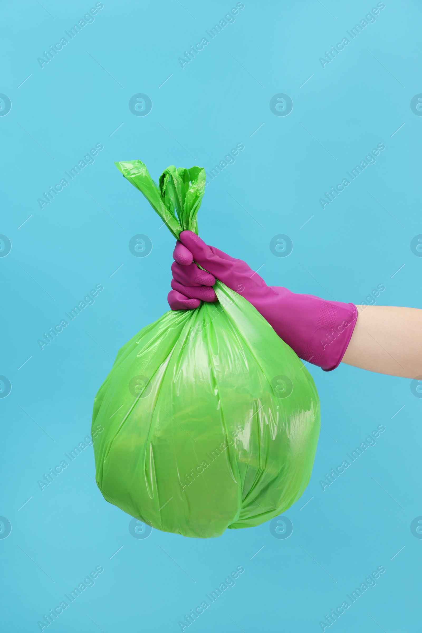 Photo of Woman holding plastic bag full of garbage on light blue background, closeup