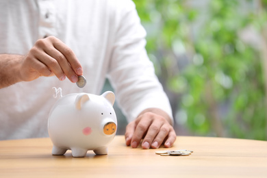 Photo of Man putting money into piggy bank at table, closeup. Space for text