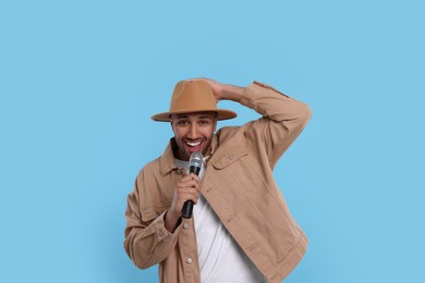 Photo of Handsome man with microphone singing on light blue background