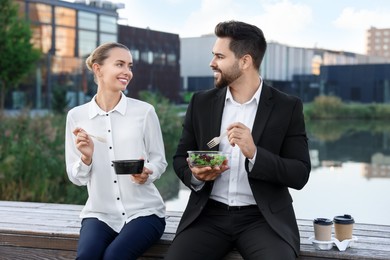 Photo of Smiling business people eating from lunch boxes outdoors