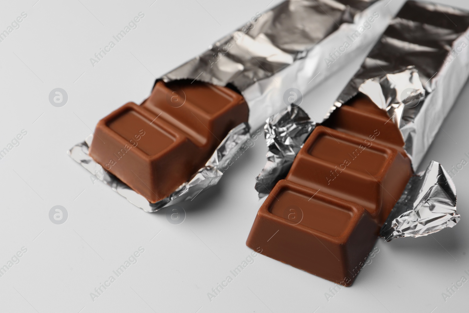 Photo of Delicious chocolate bars wrapped in foil on light blue background, closeup