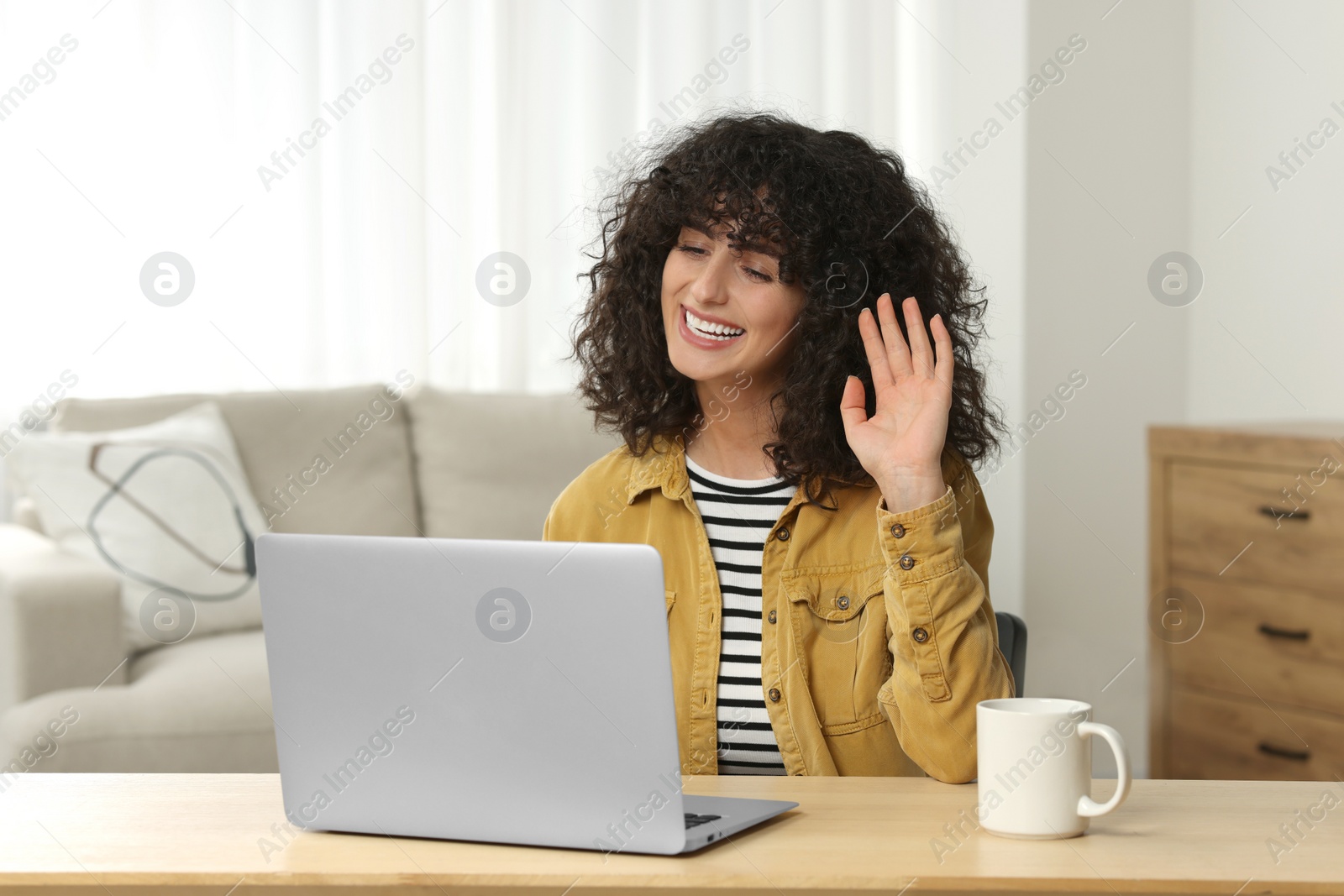 Photo of Happy woman waving hello during video call at table in room