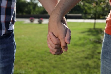 Photo of Gay couple holding hands together in park on sunny day, closeup