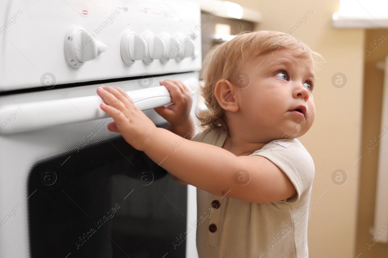 Photo of Little child playing with gas stove indoors. Dangers in kitchen