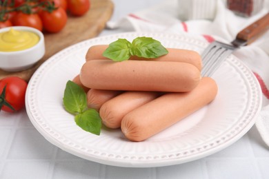 Photo of Delicious boiled sausages and basil on white tiled table, closeup