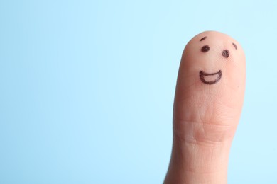 Photo of Finger with drawing of happy face on light blue background. Space for text