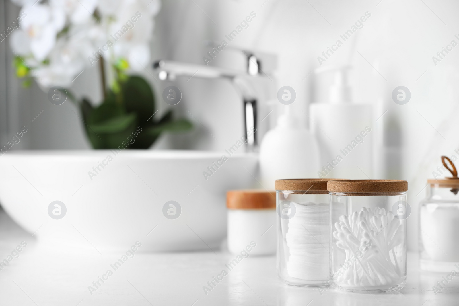 Photo of Glass jars with cotton pads and swabs on white countertop in bathroom. Space for text