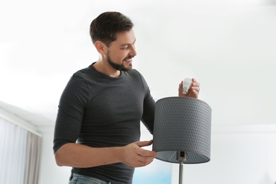 Man changing light bulb in lamp indoors